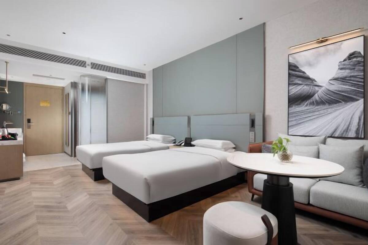 Ein modernes Hotelzimmer mit zwei Betten, einem Sofa, einem runden Tisch und einem großen Wandbild.