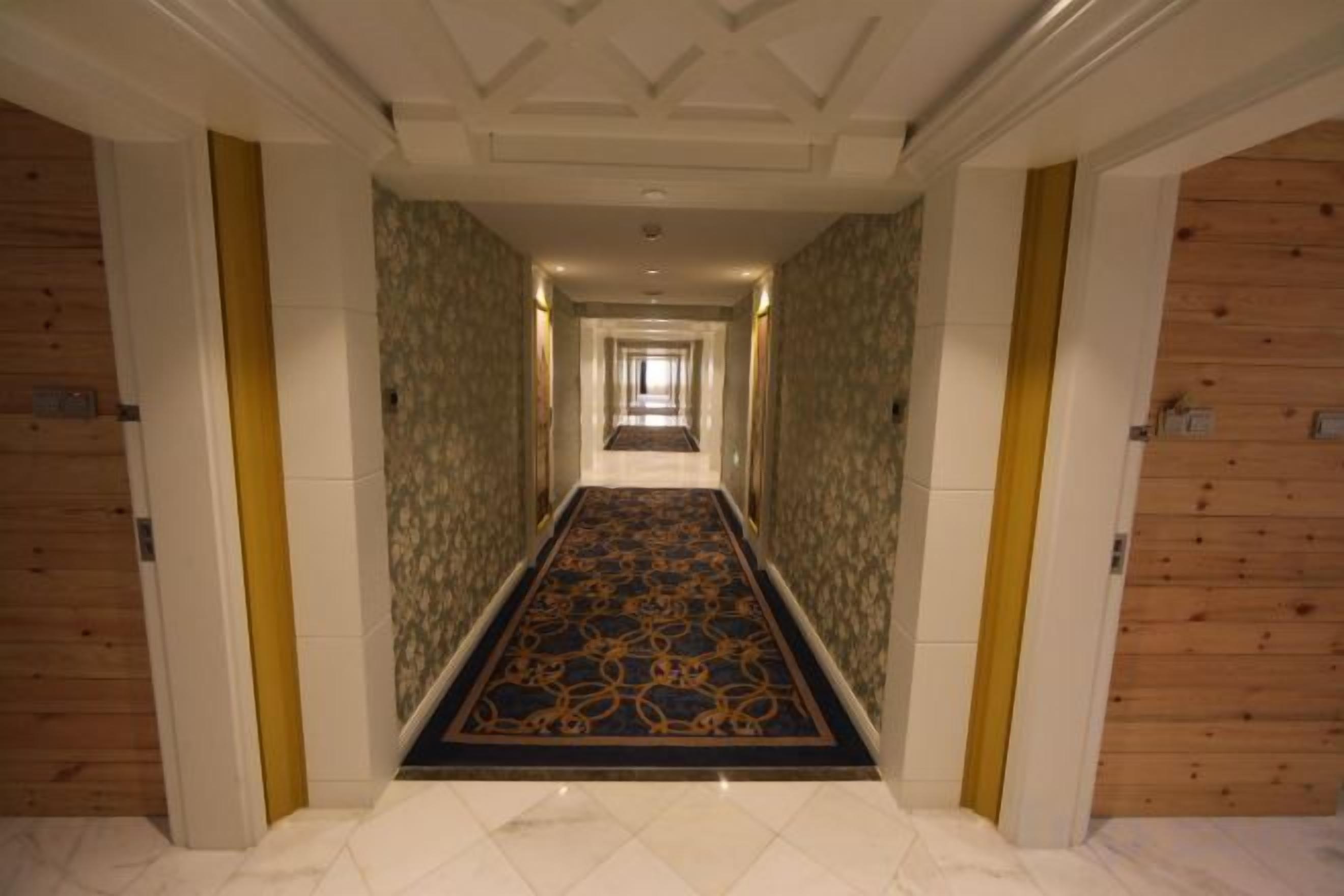 A hotel corridor with a patterned carpet, wooden panel walls, and a tiled floor.