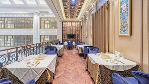 A restaurant with a long, narrow layout, high ceilings, and a herringbone floor pattern. Tables are set with white tablecloths and blue chairs. - Shunhe Zaozhuang Hotel (Zaozhuang)