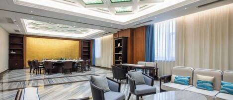 Un amplio vestíbulo de hotel con techo alto, zona de comedor, disposiciones para sentarse y un gran ventanal con cortinas.