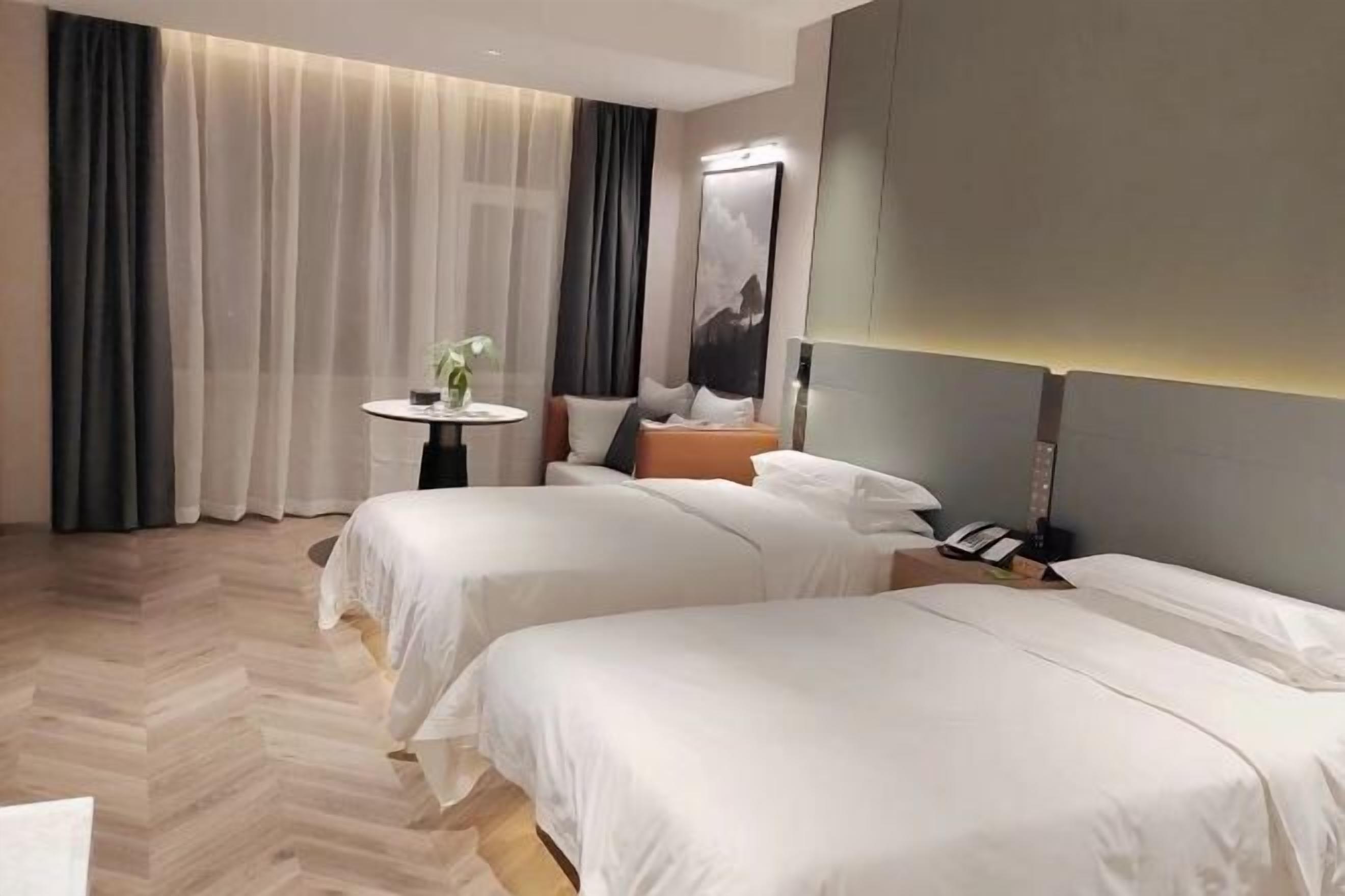 Habitación de hotel con dos camas, una mesita redonda pequeña, una mesita de noche y un ventanal grande con cortinas.