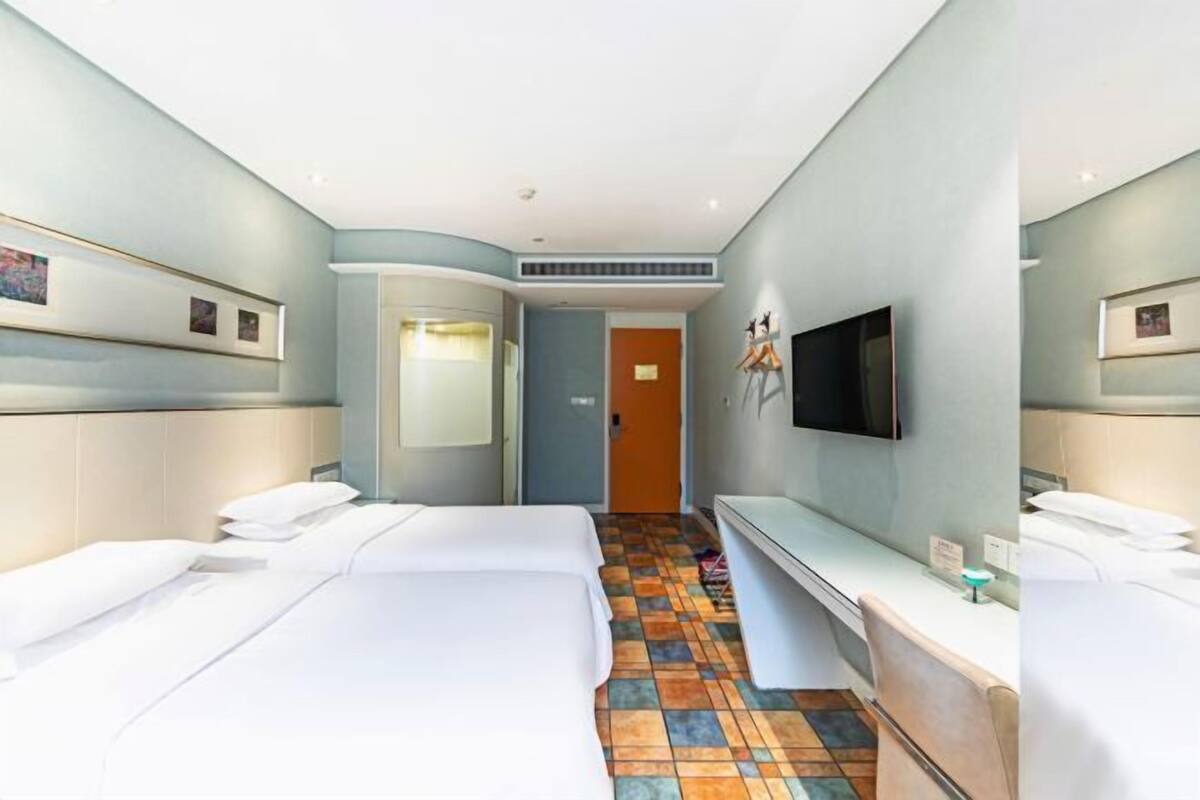 Ein Hotelzimmer mit zwei Betten, einem Fernseher, einem Schreibtisch und einer Badezimmertür.