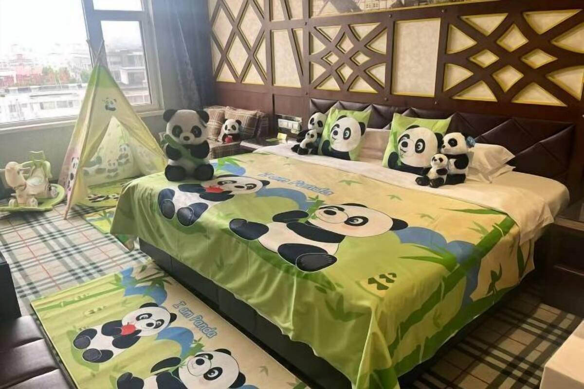 Ein Hotelzimmer mit einem Panda-Dessin bezogenem Bett, einem Fenster mit Blick auf Gebäude und einer dekorativen Wandverkleidung.