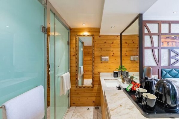 A modern bathroom with a glass shower enclosure, wooden panel walls, a large mirror, and a countertop with a kettle and coffee maker. - Shunhe Zaozhuang Hotel (Zaozhuang)