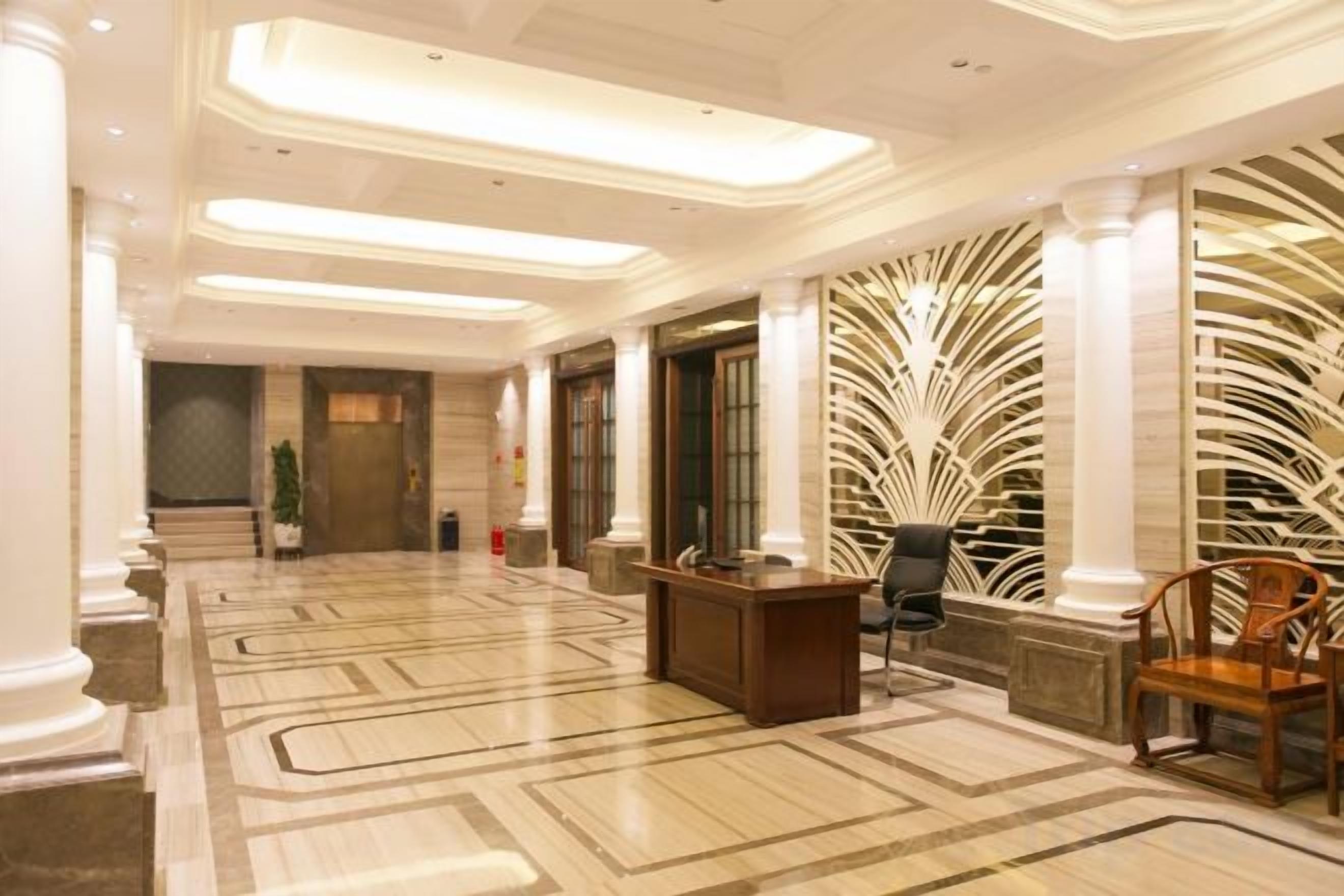 A hotel lobby with a marble floor, a reception desk, and a decorative wall.