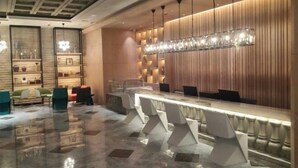 A modern hotel lobby with a long reception desk, comfortable seating, and a decorative light fixture. - Shunhe Zaozhuang Hotel (Zaozhuang)