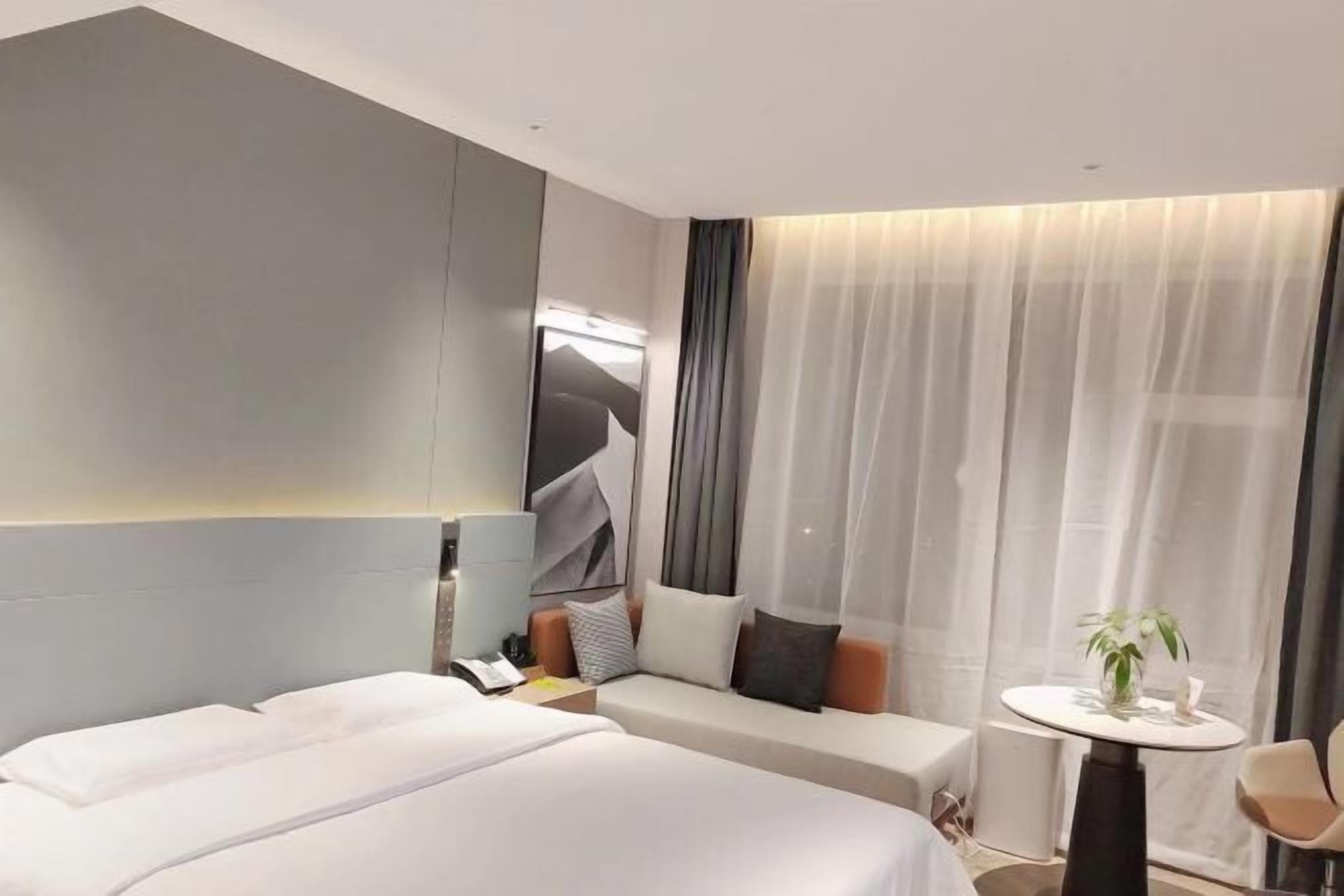 A hotel room with two beds, a sofa, a small table with a plant, and a large window with curtains.