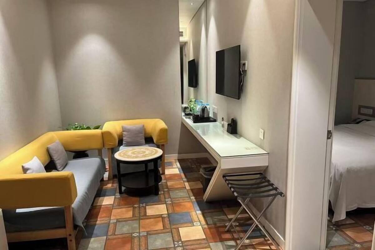 Ein kompaktes Hotelzimmer mit einer Schlafcouch, einem kleinen runden Tisch, einem Schreibtisch mit Stuhl, einem Bett und einem an der Wand befestigten Fernseher.