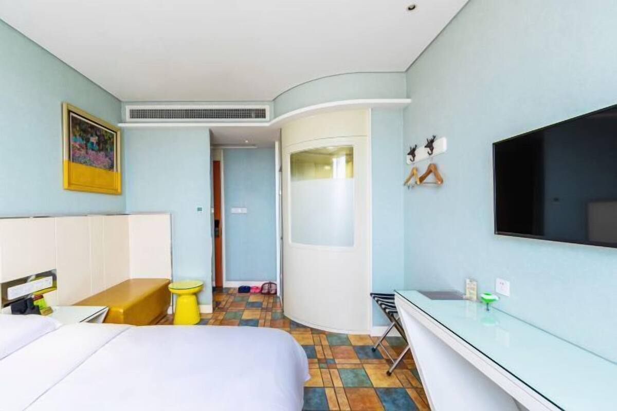Ein Hotelzimmer mit einem Bett, einem kleinen Schreibtisch, einem Fernseher, einem Badezimmer und einem farbenfrohen Fliesenboden.
