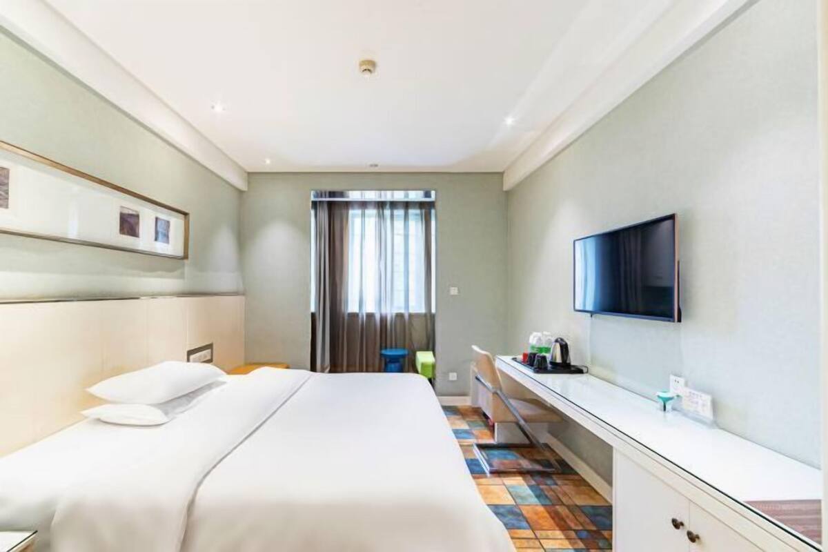 Ein Hotelzimmer mit Bett, Schreibtisch, Fernseher und einem Fenster mit Vorhängen.