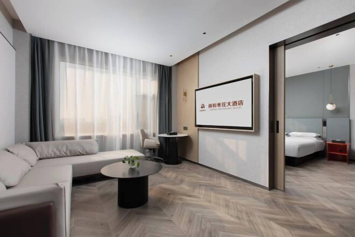Ein modernes Hotelzimmer mit einer Couch, einem Couchtisch, einem Bett und einem großen Bildschirm an der Wand.