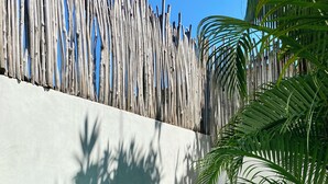 A swimming pool with clear blue water, a tiled edge, and a white wall with a bamboo fence. - Casa Coconut (Brisas de Zicatela)