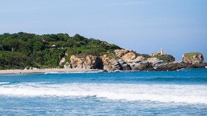 A beach with clear blue water, a sandy shore, and rocky cliffs with vegetation. - Casa Coconut (Brisas de Zicatela)