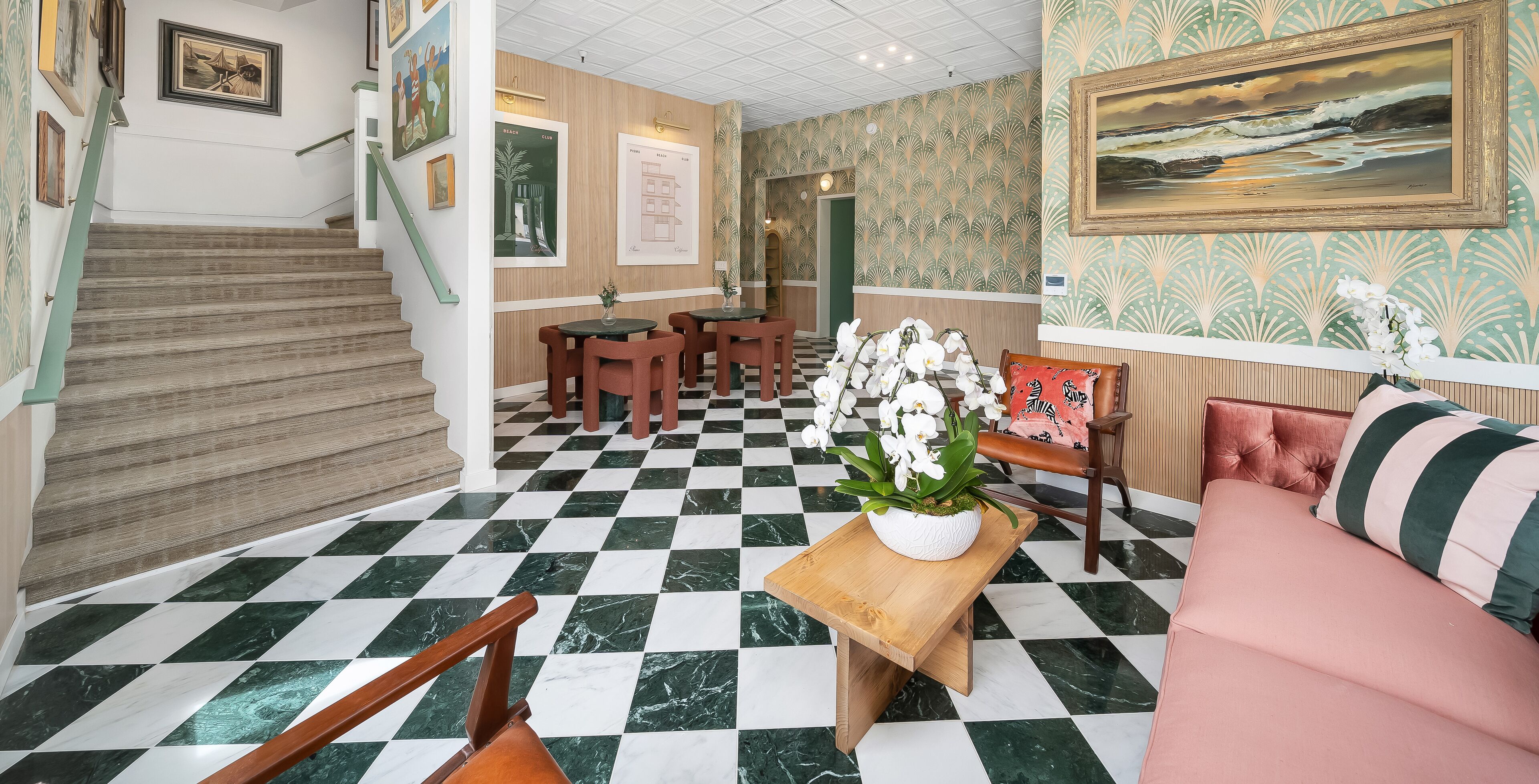 A lobby with a checkered floor, wooden staircase, seating area with tables and chairs, and a sofa.