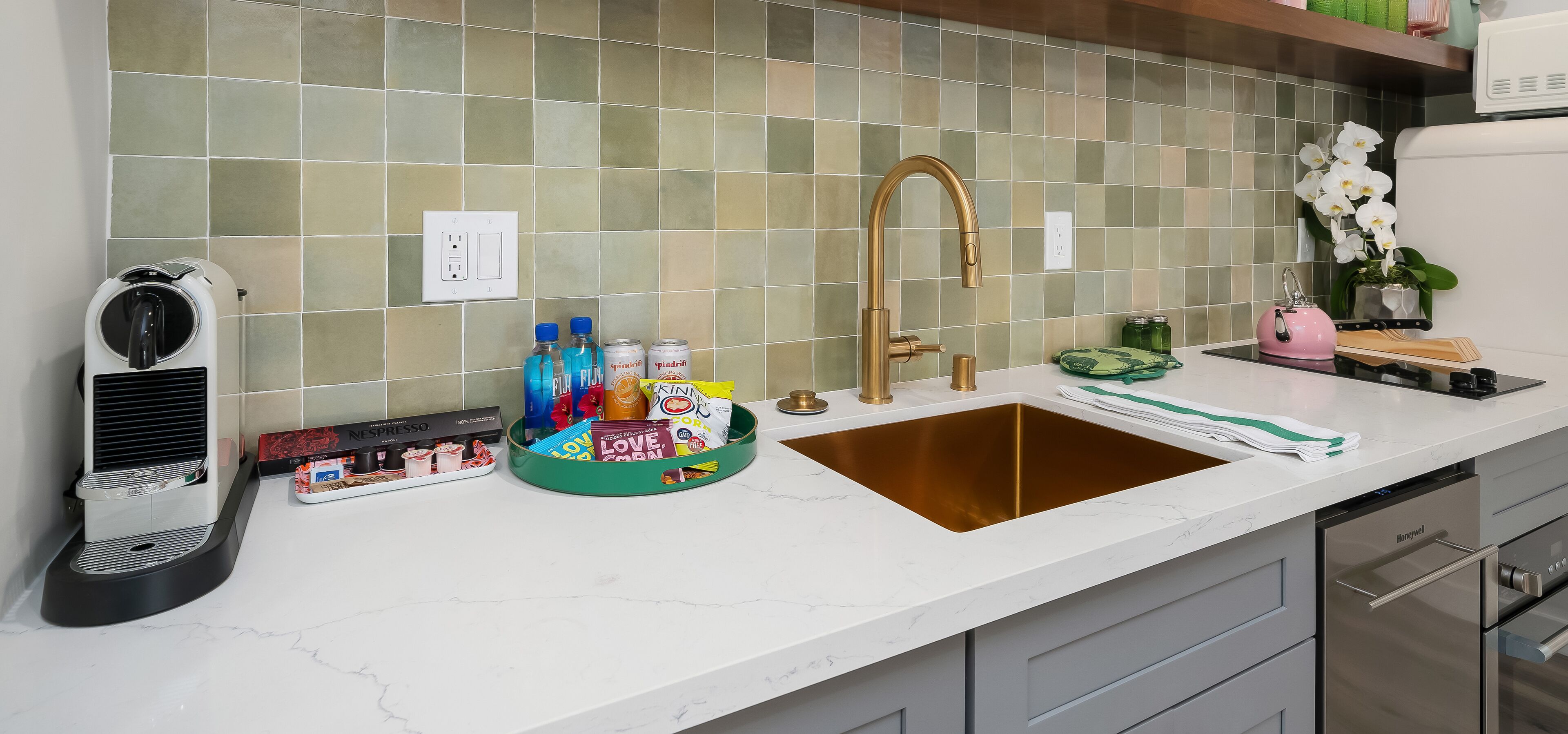A kitchen with a white countertop, a gold sink, and a coffee machine.