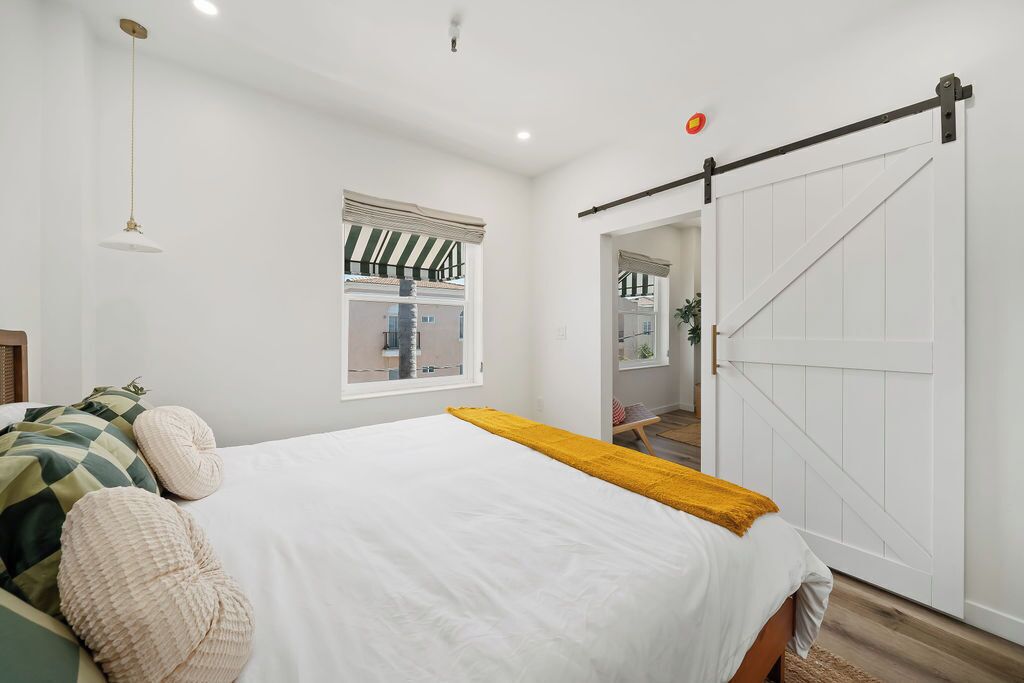 A bedroom with a bed, a window with curtains, a sliding door, and a hanging light fixture.