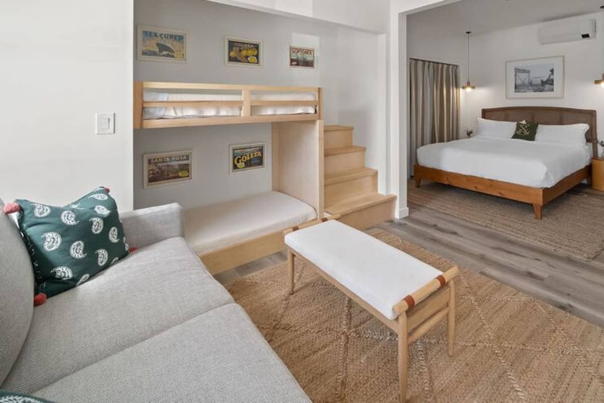 Una habitación de hotel moderna con una cama litera, una cama individual, un sofá, una mesita y un escritorio.