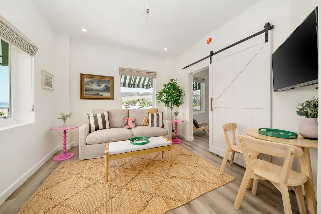 Uma sala de estar moderna com sofá, mesa de centro, televisão fixada na parede e uma porta deslizante que dá para outro ambiente.