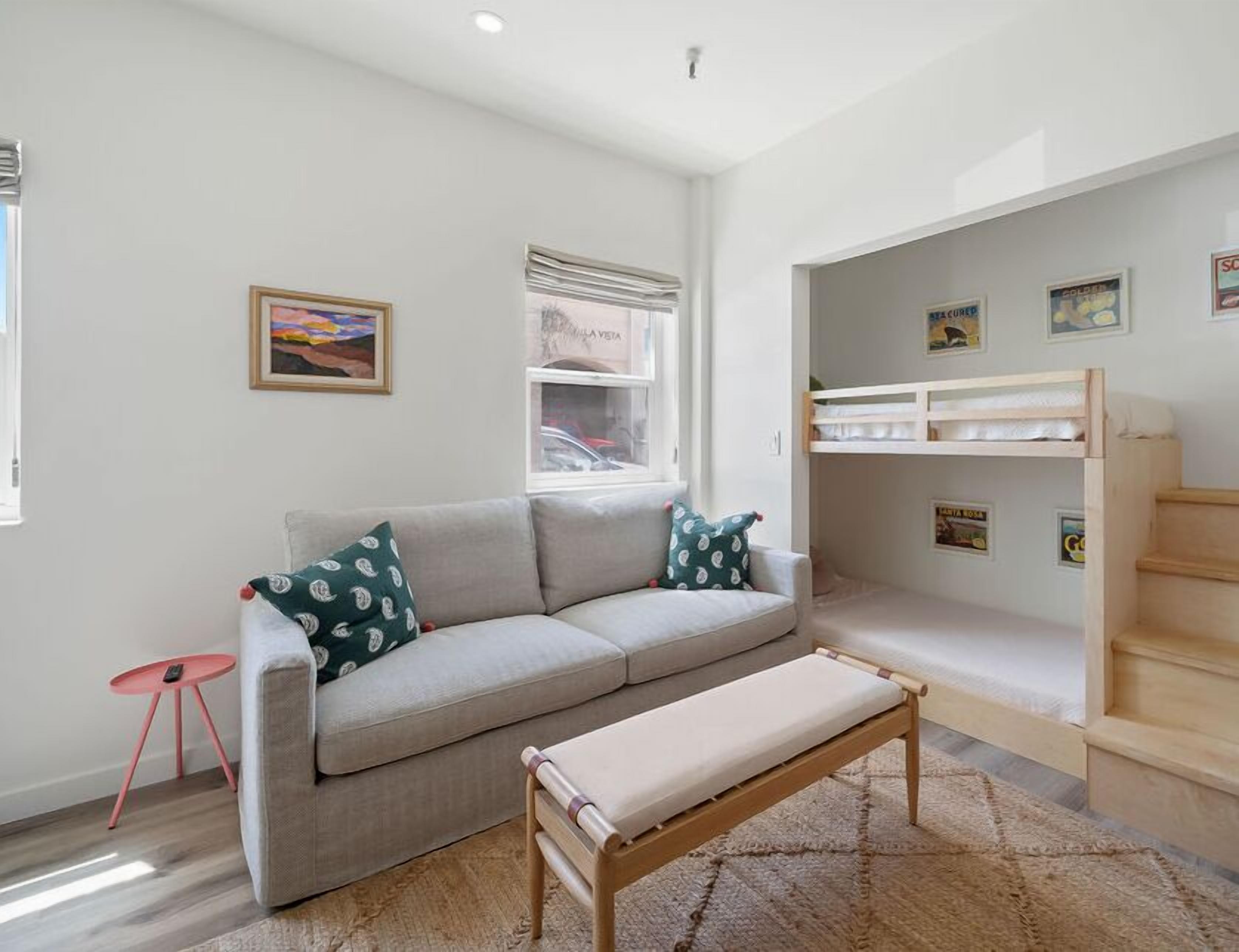 Una sala moderna con un sofá gris, un banco de madera y una cama litera.