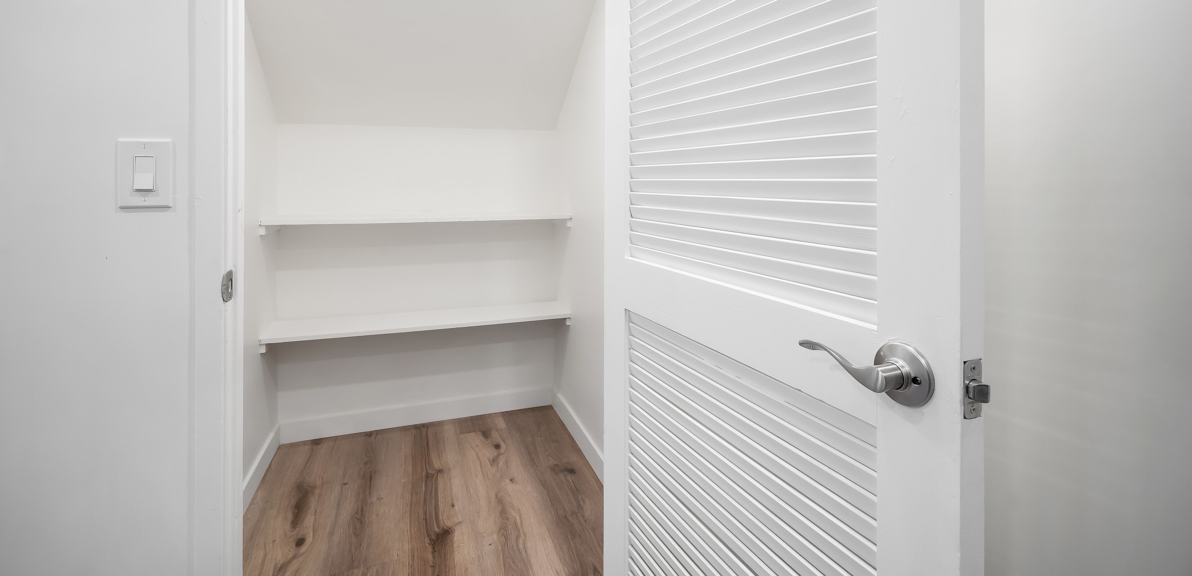 A hallway with a white door, a light switch, and a shelf unit.