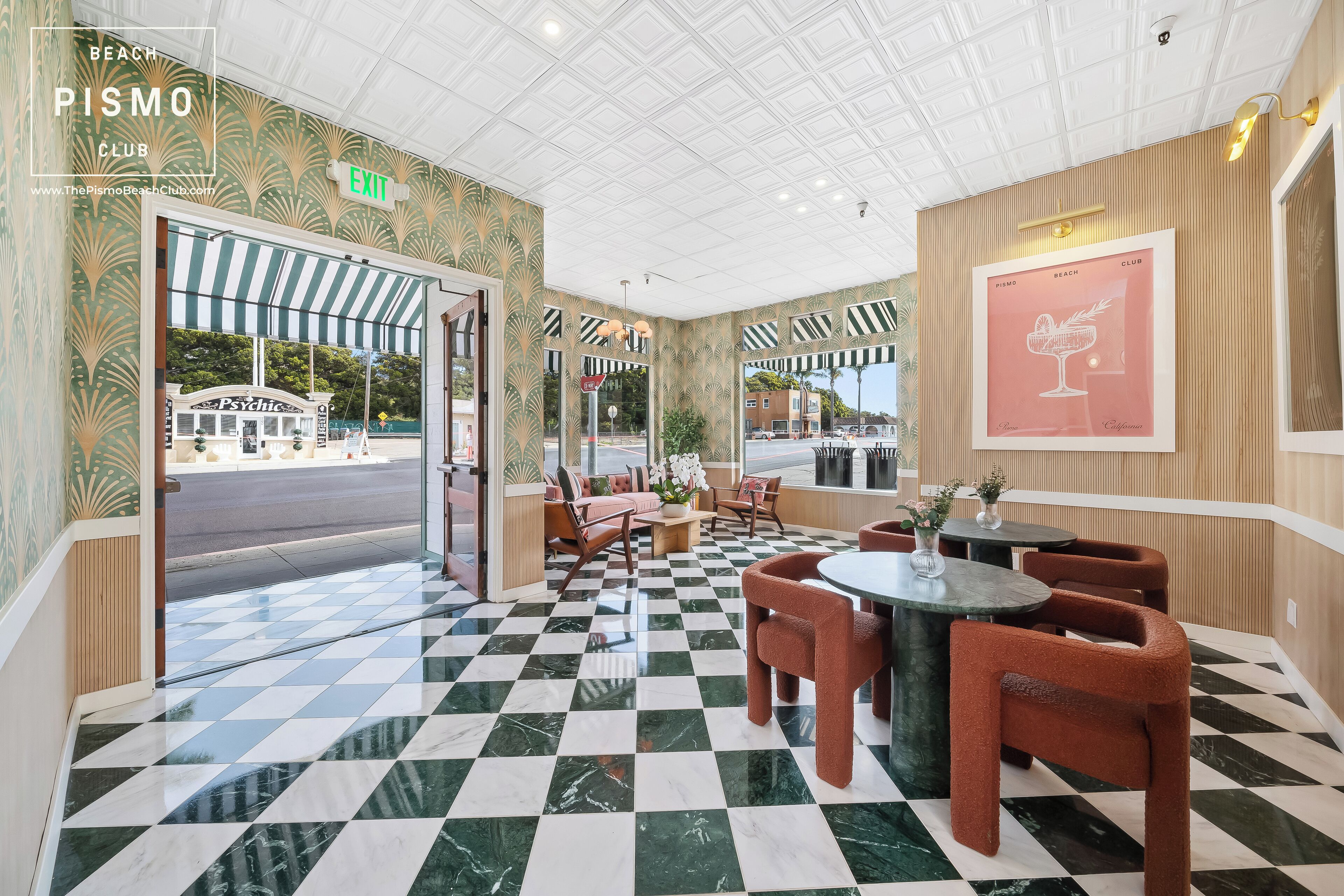 A beach club interior with checkered flooring, seating areas, and a view of the street outside.