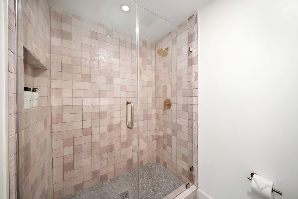 Eine Dusche mit Glastür, gefliesten Wänden und einer Handstange.