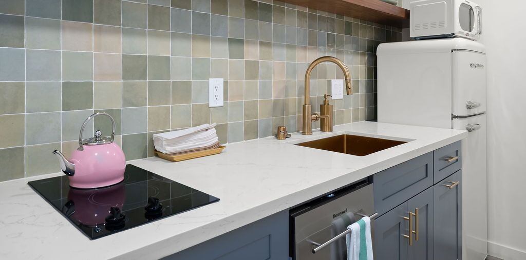 A kitchen with a pink kettle, a sink, a microwave, and a dishwasher.