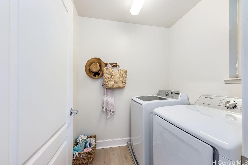 A laundry room with two washing machines, a basket with clothes, a hat, and a woven bag on the wall.