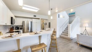 A modern kitchen with white cabinets, stainless steel appliances, and a central island with stools. - Charming and immaculate, fully furnished 3-bedroom 3 bath townhouse in Ko'Olina! (Kapolei)