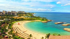 A beach resort with a sandy shoreline, clear turquoise waters, and a backdrop of hotels and palm trees. - Charming and immaculate, fully furnished 3-bedroom 3 bath townhouse in Ko'Olina! (Kapolei)