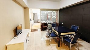 A modern dining area with a black table and blue chairs, a TV on a white cabinet, and a view through a glass partition to another room. - Wanjia Hotel (Lincang)
