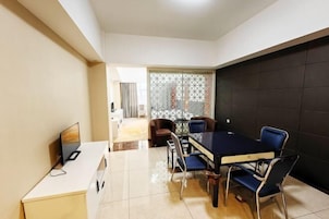 Un comedor moderno con una mesa negra y sillas azules, un televisor sobre un mueble blanco, y vistas a otra habitación a través de un separador.