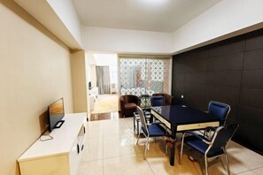 Un comedor moderno con una mesa negra y sillas azules, un televisor sobre un mueble blanco, y vistas a otra habitación a través de un separador.
