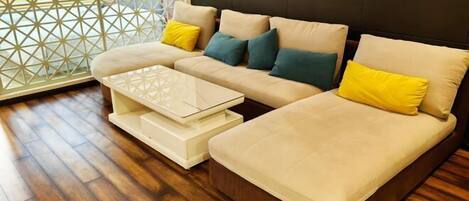 A modern living room with a sectional sofa, a glass coffee table, and a wooden floor.