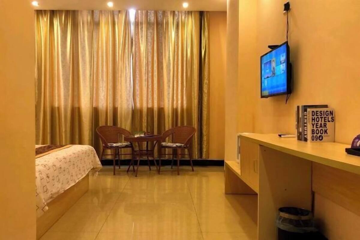 A hotel room with a bed, a desk, two chairs, a television, and a curtain.