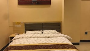 A hotel room with a bed, a nightstand, a wall-mounted artwork, and a bedspread with a pattern. - Qingyuan Dongguan Fengxiang Hotel (Lianzhou)