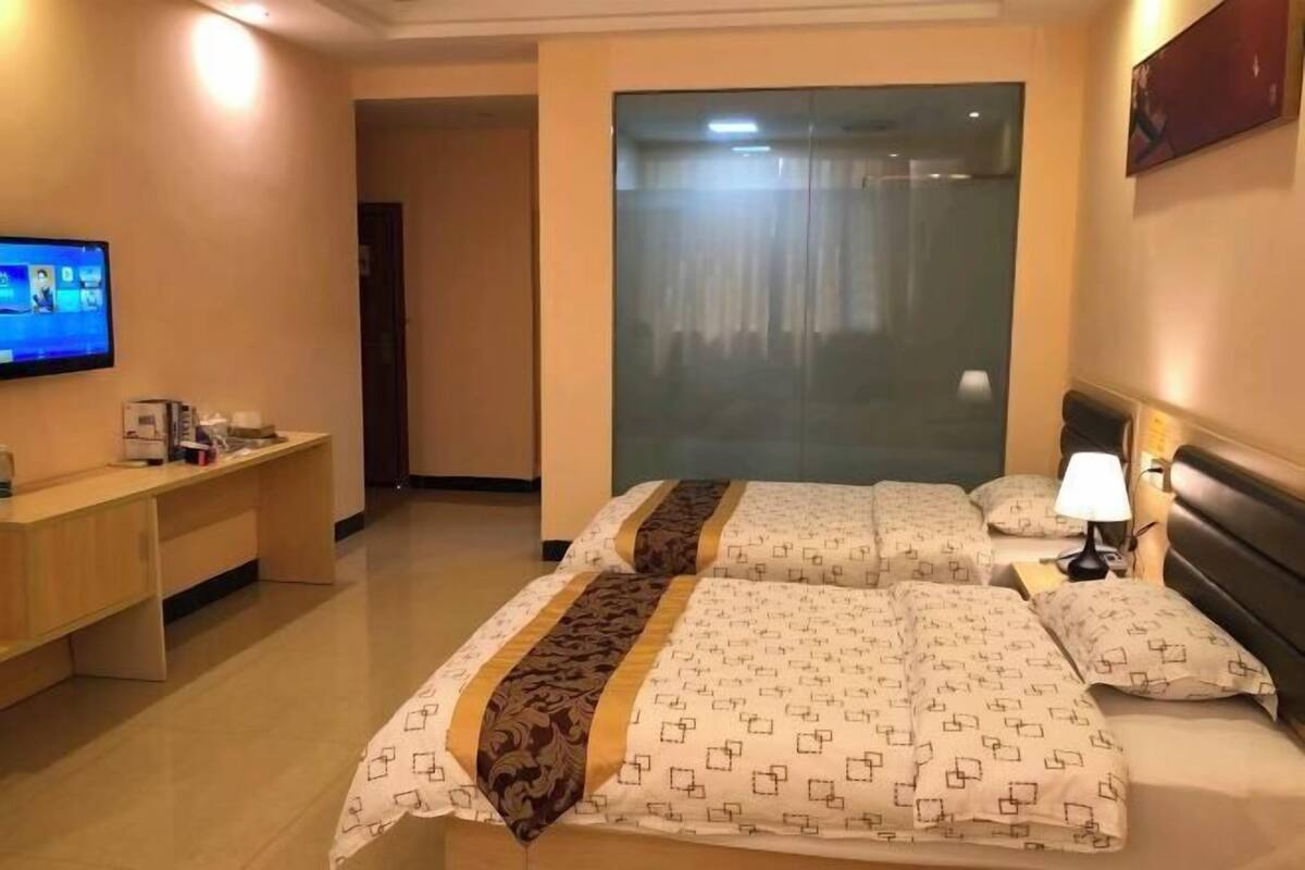 A hotel room with a bed, bedside table, lamp, TV, and a desk with a chair.