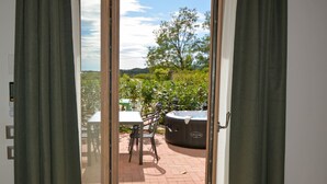 A patio with a table and chairs, a hot tub, and a view of greenery and hills. - Residence Corte Bellebarbe - Il Volto (rivoli veronese)