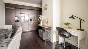Een moderne keuken met donkere kastjes, een eethoek met een witte tafel en stoelen, en een werkplek met een bureau en stoel.