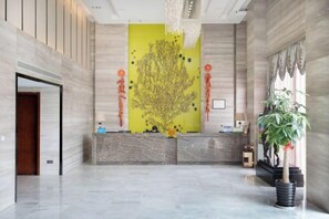 A lobby with a reception desk, a large yellow artwork, and a potted plant.