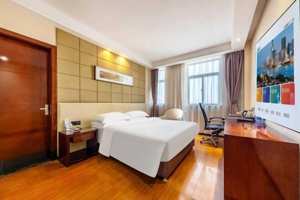 Une chambre d’hôtel avec un lit, une table de chevet, une chaise, un bureau et une grande fenêtre.