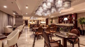 A hotel lobby with a marble floor, multiple dining tables with chairs, a reception desk, and a patterned ceiling. - Wan Yue Hotel (Jinjiang)