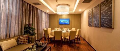 A modern dining area with a round table set for six, a sofa with a tray of teapots, and a television on the wall.