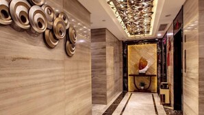 A modern hotel lobby with marble flooring, a decorative ceiling, and a reception area with a plant and a small table. - Wan Yue Hotel (Jinjiang)