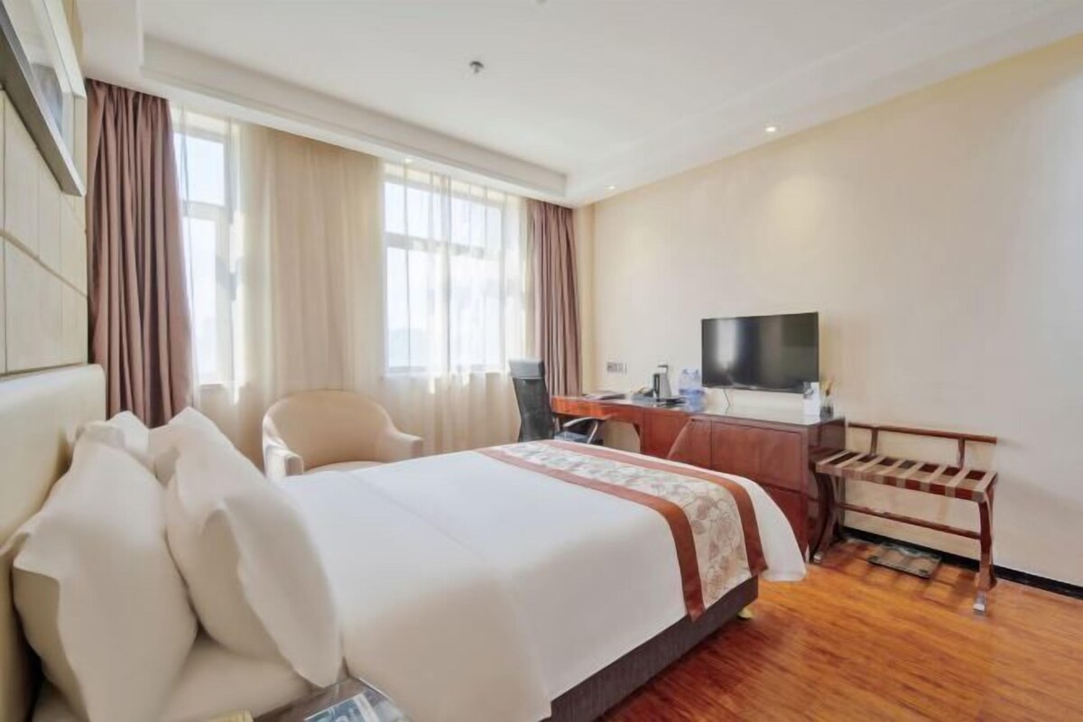 A hotel room with a large bed, a desk, a chair, a television, and a window with curtains.