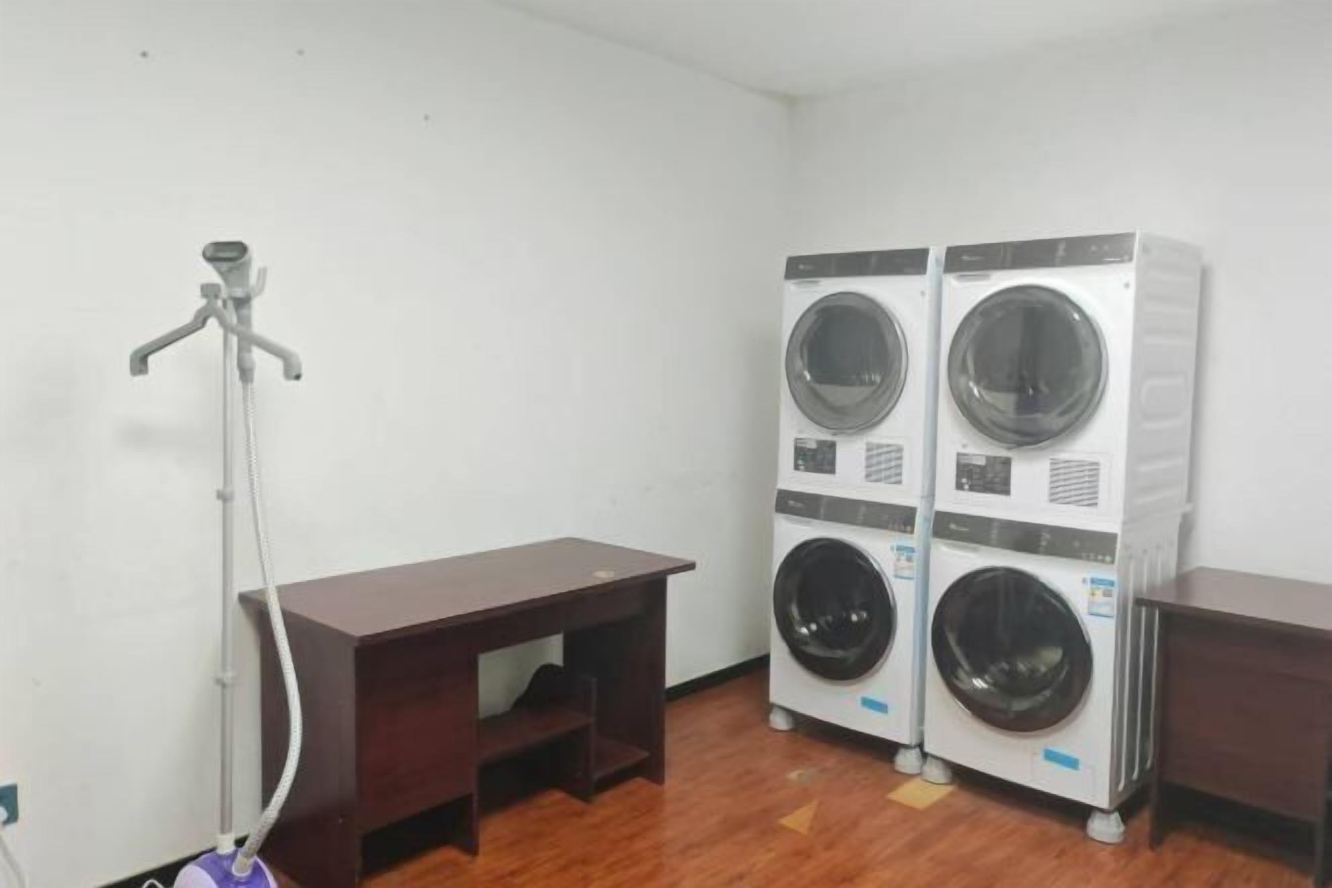 A laundry room with two stacked front-loading washing machines, a wooden desk, and a floor-mounted washing machine.