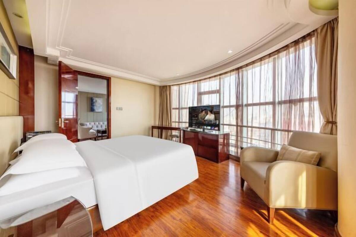 Une chambre d’hôtel avec un lit, un canapé, un bureau avec une télévision et de grandes fenêtres.
