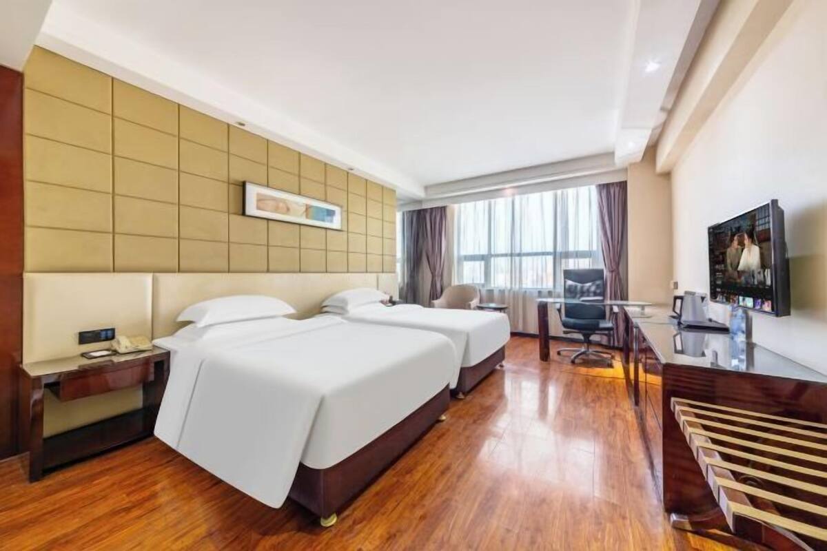 Une chambre d’hôtel avec deux lits, un bureau, une chaise, une télévision et une grande fenêtre.
