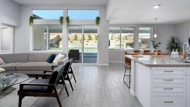 Une cuisine moderne dotée d’un grand îlot central, un coin repas avec une table en verre et un salon avec un canapé et des fauteuils.
