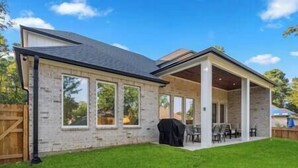 Ein Haus mit überdachter Terrasse, Backsteinfassade und Rasen.